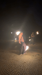 Fire dancers perform nighttime torch spinning demonstration in paved area