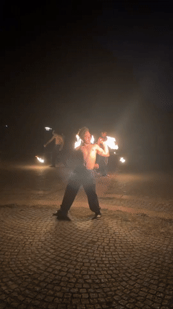 Fire dancers perform nighttime torch spinning demonstration in paved area