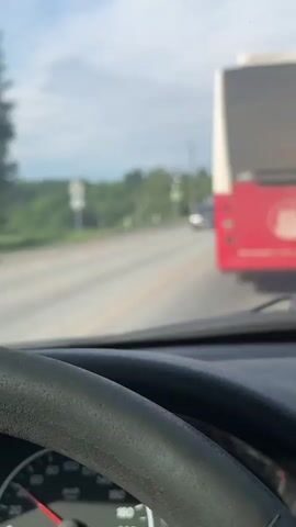 The video is filmed from inside a car, showing the view through the windshield over the steering wheel and dashboard. The car is driving on a paved road, following a red and white bus.

At the beginning, a gray car approaches and passes in the opposite lane. As the car continues, a white Foton truck, followed by another white truck, also pass in the opposing lane.

The setting appears to be a rural or semi-rural area, with green trees lining the road on both sides. Power lines run parallel to the road. A yellow triangular road sign with a black "A" (indicating a pedestrian crossing) is visible on the left side of the road.

The bus in front has "КЛИМАТ" (Klimat) and "LIAZ" visible on its rear. The Foton truck has the model name "FOTON" on its grille and a partial license plate "Н971УУ43". The time of day is bright, with a sky that is partly cloudy. The speedometer of the recording car is partially visible, showing "km/h" markings.