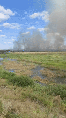 Field fire sends up heavy smoke over a rural wetland area