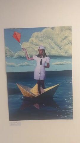 The video shows a pan across three framed artworks hanging on a white wall. The first artwork on the left is a painting of a woman in a sailor outfit standing in a paper boat in the ocean, holding a red kite. The middle artwork is a photograph of a woman's head in profile wearing an orange headdress and elaborate eye makeup. The third artwork on the right is a photograph of a woman's face, partially obscured by a dark, netted veil and colorful makeup.