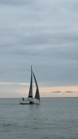 Sailboat cruising calm Batumi waters under a cloudy sky