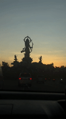 Driver records statue at Denpasar roundabout during colorful sky