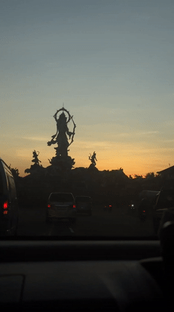 Driver records statue at Denpasar roundabout during colorful sky