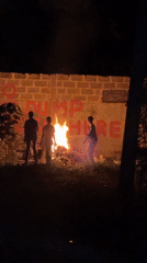 Three people gather around nighttime bonfire in Ajara, Nigeria