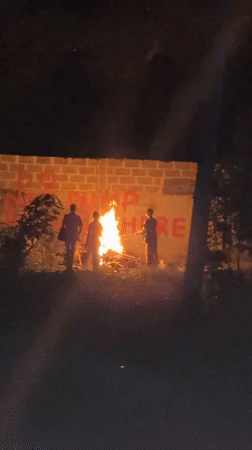 Three people gather around nighttime bonfire in Ajara, Nigeria