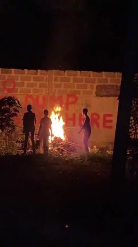 Three people gather around nighttime bonfire in Ajara, Nigeria