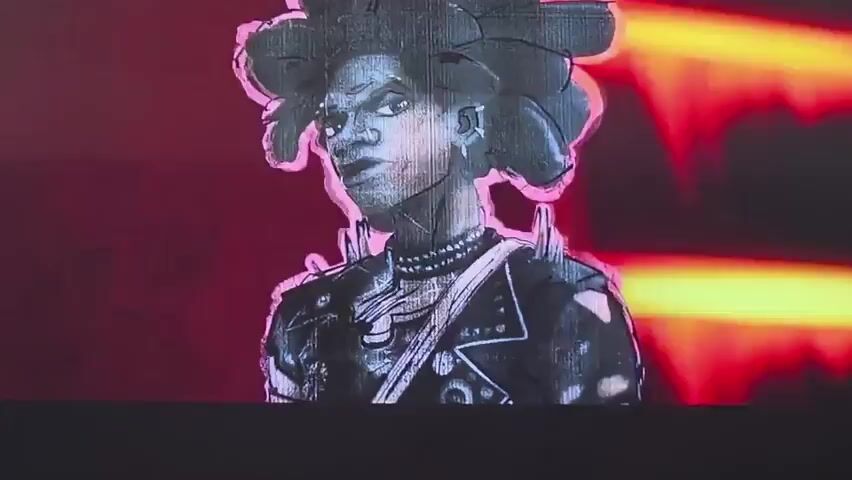 The media file features two distinct visual segments, presented in sequence. The first segment, lasting from 00:00 to 00:01 and again from 00:03 to 00:04, displays a stylized, black-and-white animated portrait of a person with a large, spiky afro hairstyle. This individual wears a studded jacket and a choker necklace. A thin pink outline encircles the figure and its hair. The animation style is reminiscent of a sketch or drawing, with visible lines and textures.

The second segment, spanning from 00:01 to 00:03, presents a scene from an animated film. A young person, identified by their black suit with a red spider emblem on the chest, stands in what appears to be an indoor setting. The lighting is dramatic, with prominent red and yellow hues, suggesting a potentially intense or futuristic environment. The character on the right has red eyes and appears to be a person of color. To the left, a portion of another character is visible, rendered in a more textured, possibly grayscale style, with patterned clothing. The overall mood of this segment is more dynamic and action-oriented compared to the static portrait.

No specific time of day, weather conditions, or external location cues are evident. The emotion conveyed by the animated character in the second segment appears neutral or slightly curious. There is no visible text in either segment of the media file. The provided location context of Vozrozhdeniye, Russia, does not appear to be directly represented by any visual elements within the media.