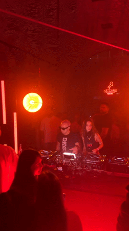 Red-lit Warsaw club night, DJ booth and dancing crowd.