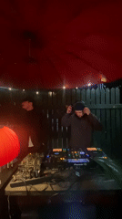 DJs perform outdoor nighttime set under red umbrella with lights
