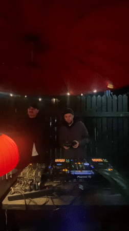 DJs perform outdoor nighttime set under red umbrella with lights