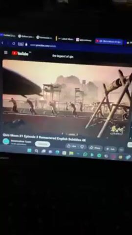 Here is a concise description of the video: 

The video shows a person watching an episode of the animated series “Qin’s Moon” on their laptop. The episode being watched is titled "Qin’s Moon S1 Episode 3 Remastered English Subtitles 4K". The scene displays what looks like soldiers on a watch tower, but they appear to be chained to some contraption and running. The YouTube interface is visible around the video, along with other open tabs at the top of the screen.  The laptop is a Lenovo model.