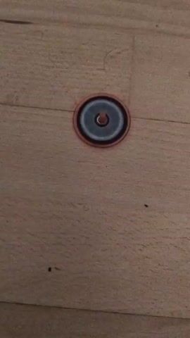 A close-up, overhead shot shows a red and black fidget spinner with a silver center spinning on a light brown wooden floor. The spinner is centered in the frame.