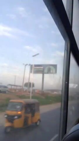 The video is filmed from inside a vehicle, looking out the side window. The view shows a road with a motorcycle passing by on the left. There is a billboard in the distance that reads "OPay The Digital Bank Nigeria Trusts". There are also utility poles and some buildings in the background. The sky is blue with some clouds. The video is shaky, suggesting the vehicle is in motion.