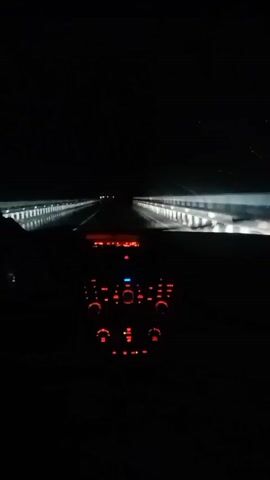 The video shows the interior of a car driving at night on a road. The dashboard lights are illuminated in red. The road ahead is dark with some lights visible in the distance. The camera is looking forward through the windshield. The image is slightly blurry due to the movement of the car.