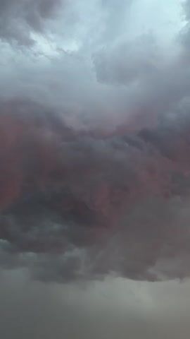 This video captures a close-up view of turbulent, dark gray and pinkish-purple storm clouds against a bright, overcast sky. The lighting suggests either an approaching or receding storm. There are no people or objects visible, and the focus remains solely on the dramatic cloud formations. The environment is an outdoor sky.