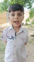 Boy in pink shirt plays outdoors, cows feed nearby