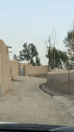 Vehicle drives through rural Kandahar street among traditional buildings