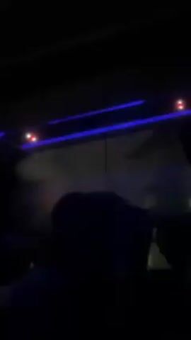 The video shows a dimly lit interior, possibly of a vehicle, with blue LED strip lights lining the ceiling and small red lights also visible. The silhouette of a person is noticeable in the lower portion of the frame. The outside is visible through the window, although obscured, suggesting movement of the vehicle. The overall ambiance is dark and blue-toned.
