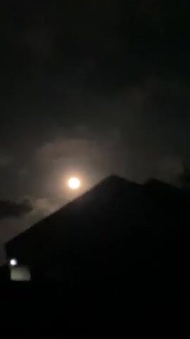 A still shot shows a full moon in a cloudy night sky, with the silhouette of a pitched roof in the foreground. A faint light is visible on the left side of the roof.