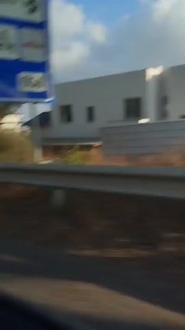 This is a close-up, first-person perspective video taken from the backseat of a vehicle. The focus is on the back of the front seat, which has a black mesh pocket. Below the seat, a person's legs and feet are visible, wearing light-colored pants. The person is shifting their weight, causing the camera to move. The environment appears to be a car interior, with the lighting suggesting daytime.