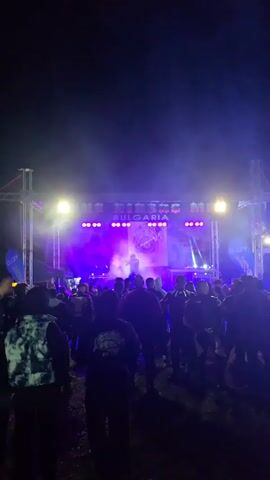 Here is a description of the video:

The video shows a concert at night. A performer is visible on stage, under bright purple and white lights. The background features a sign that says "MR. BIKER BULGARIA RIDE 2024" and an emblem. The crowd is silhouetted in the dark. In one moment, the camera is briefly aimed upward, capturing a bright light source.