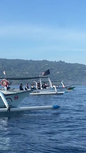 Outrigger boats ferry passengers toward mountain in Banjar waters