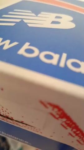 The video is a close-up, low-angle shot of a blue and white New Balance shoe box. The New Balance logo, a stylized "NB" with horizontal lines, is prominently displayed in white on the blue surface. The word "balance" is partially visible in white lettering below the logo. The box appears to be made of cardboard. The camera is slightly out of focus, giving the image a soft, blurred effect. The lighting is dim, suggesting it might be indoors or nighttime. There are no people visible, and the overall mood is neutral. The provided location context is Donetsk, Ukraine, but there are no specific visual cues in the video to confirm this.