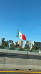 Mexican flag waves between highway and Mexico City skyline