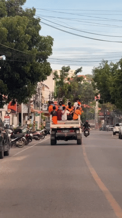 Group in orange shirts rides flatbed truck through Choeng Mon