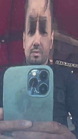 A man takes a selfie in a teapot. The initial shot shows the man holding the phone, facing the camera. The following shot shows the teapot on a decorative silver platter, with the man's distorted reflection visible on the teapot's surface. The final shot reveals the teapot, cup, sugar, and water bottle on a table indoors, with a street scene of palm trees and cars visible through the window.