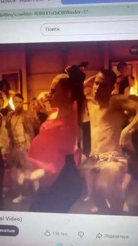 The video shows a group of people dancing. In the first frame, a woman with dark hair is dancing with her arms raised, wearing a pink shirt and dark pants. A man with dark hair and a beard is dancing behind her. In the second frame, a person with curly hair is bent over, dancing. To their right, a man with a beard and a patterned shirt is dancing. In the third frame, a woman with blonde hair is dancing with her arms outstretched. In the fourth frame, a person in a red shirt is seen from the waist down. The background appears to be a dimly lit indoor space in the first three frames and an outdoor setting with a cloudy sky in the last frame.