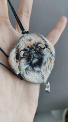 Person displays embroidered Pekingese dog pendant in Ust-Ilimsk