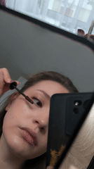 Woman applies mascara while looking in mirror