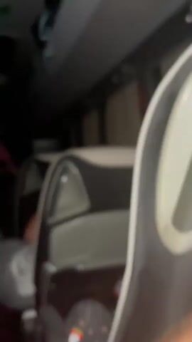 The video depicts the interior of a bus at night. The lighting is dim, with green lights highlighting the ceiling. Several passengers are visible, some sitting and others walking through the aisle. The seats are white and grey, and there's overhead storage space. Music is playing in the background.