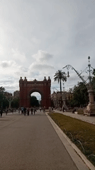 Pedestrians gather at historic Barcelona archway with street musician