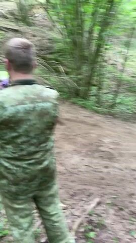 The video shows a person riding a dirt bike up a dirt track in a forest. The rider is wearing a red helmet and a white shirt. The track is surrounded by green trees and bushes. The camera is held by a person standing on the side of the track. The rider makes a sound like revving an engine.