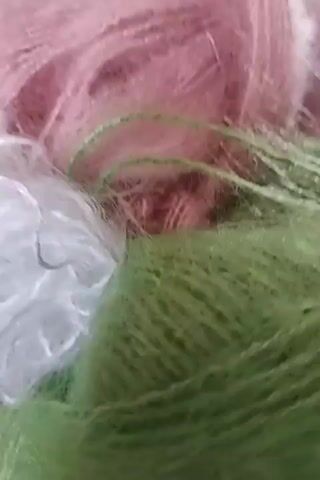 The video shows balls of yarn in pink, white, and green. Then, it shows a close-up of a pink knitted sweater with embroidered white flowers and green leaves. Finally, it shows the entire sweater, revealing a loose knit pattern and various embroidered floral details across the garment.