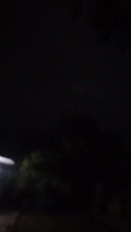 The video captures a nighttime scene. The majority of the footage is dark, with very little visible. In the second frame, there is a blurry image of what appears to be a brick wall on the right side and some dark foliage or trees on the left. A faint light, possibly a distant star or airplane, is visible in the sky in the third frame. The rest of the video is almost entirely black, suggesting the camera is facing a dark environment with minimal illumination.