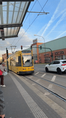 Yellow tram departs Essen stop as woman waits