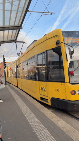Yellow tram departs Essen stop as woman waits