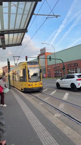 Yellow tram departs Essen stop as woman waits