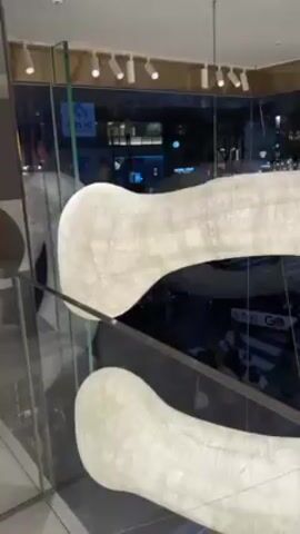 The camera pans from a view of a street outside a window to a white, abstract, hollow sculpture. Next, it shows a colorful wall mural of figures in different poses, then rotates to a display of handbags in a store.