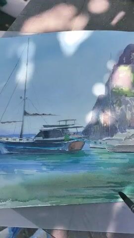 A watercolor painting of a bay with boats and a cliff is shown. The painting is on a table outdoors. There are shadows of leaves on the painting and the table.