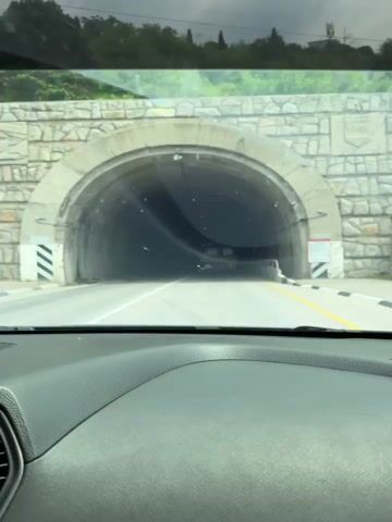 The video shows a car driving through a tunnel. The tunnel is concrete and lit by intermittent lights in the ceiling. The car drives on the right side of the road, following the white line. Another car passes in the opposite direction.
