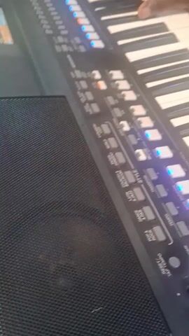 A person is playing a keyboard, which appears to be a Yamaha, with a black speaker grill on the left side. The keyboard has several buttons with blue lights illuminated. The hand of the person is visible as they play the keys. The background music is audible.