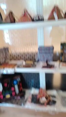 The video shows a retail display of bags and hats on white shelves. The bags and hats are various colors and patterns, with some appearing to be handmade. The display shelves are illuminated from above by what appears to be a window with frosted glass. The video pans slowly across the shelves, showing different angles of the merchandise. The video appears to be taken in a retail store or market.