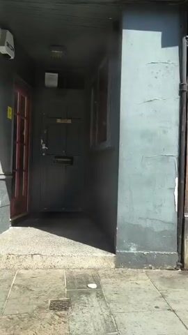 The video shows a series of shop fronts. The first shop has a dark wooden door and a window displaying clothing. The second shop has a sign that reads "ATTORNEY'S WALL." The third shop has a large glass window with a notice posted inside. The fourth shop is a pharmacy with a "Boots" logo and various signs displayed. The final shop has a white facade and a large display window. The footage appears to be taken from a moving perspective, possibly a person walking down a street. The weather appears to be sunny.