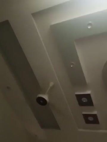 A ceiling fan with white blades is partially visible in the lower left corner of the video. The ceiling is decorated with recessed lighting and square inset panels, some of which are dark brown with a small circular light in the center. A circular vent with a patterned grille is also visible on the ceiling. The video pans across the ceiling, revealing different sections of the decorative design and the fan.