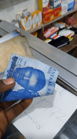 Person handles mixed Nigerian currency at counter with paperwork